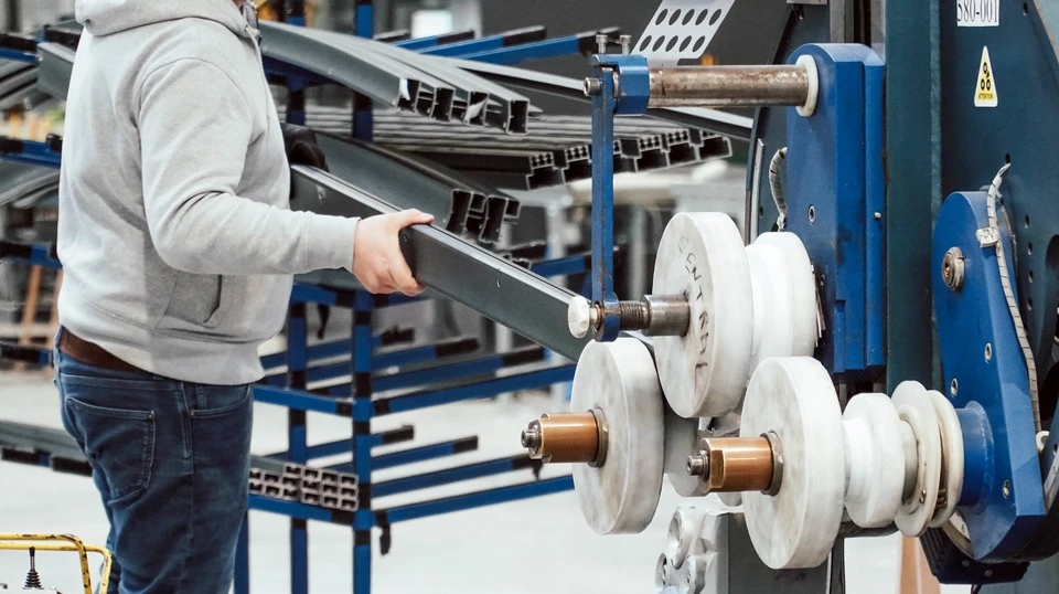 Ouvrier en atelier industriel manipulant un profilé aluminium extrudé vers une machine à rouleaux de galetage