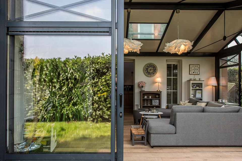 Véranda moderne avec grandes baies vitrées à profilés aluminium anthracite, donnant sur terrasse en bois composite