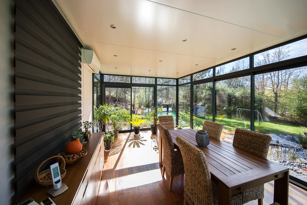 Véranda moderne avec grande baie vitrée à profilés aluminium anthracite, donnant sur jardin boisé