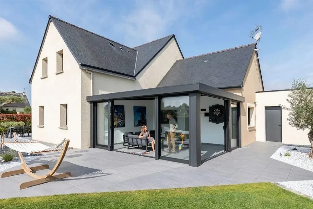 Extension moderne avec véranda aluminium gris anthracite, grandes baies vitrées coulissantes grand format, ouverte sur terrasse en lame de bois composite