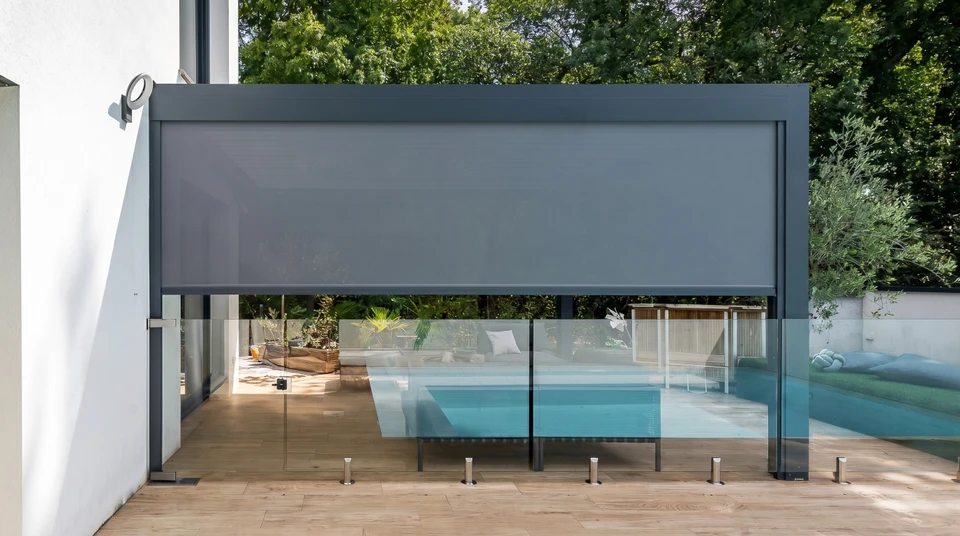 Pergola bioclimatique en aluminium anthracite, adossée à une maison, avec lames orientables en façade formant des volets coulissants